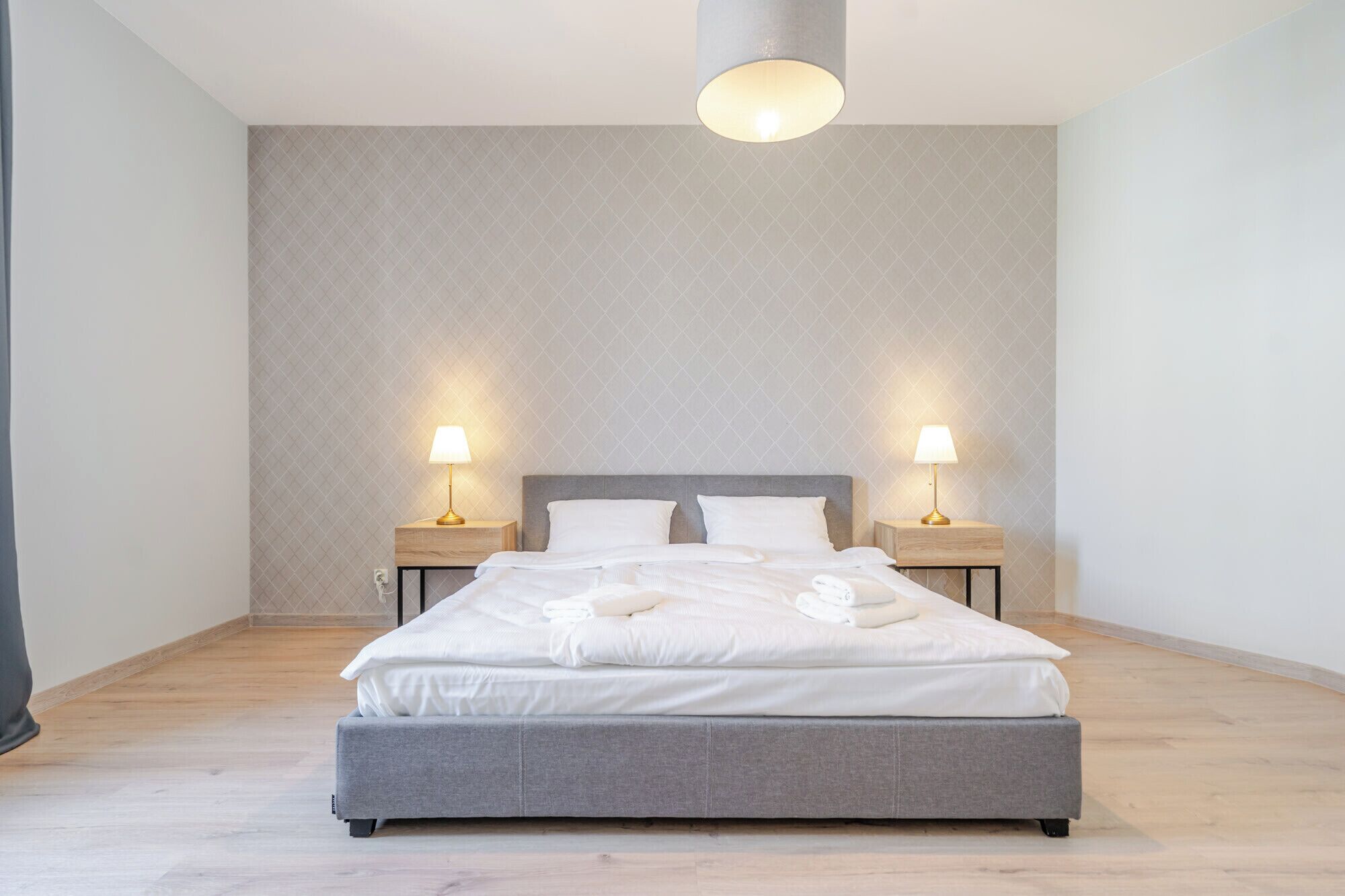 A modern bedroom with a grey bed, two bedside tables with lamps, and a patterned wall.