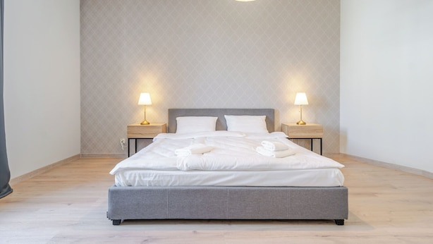 Ein modernes Schlafzimmer mit einem grauen Bett, zwei Nachttischen mit Lampen und einer Wand mit Muster.