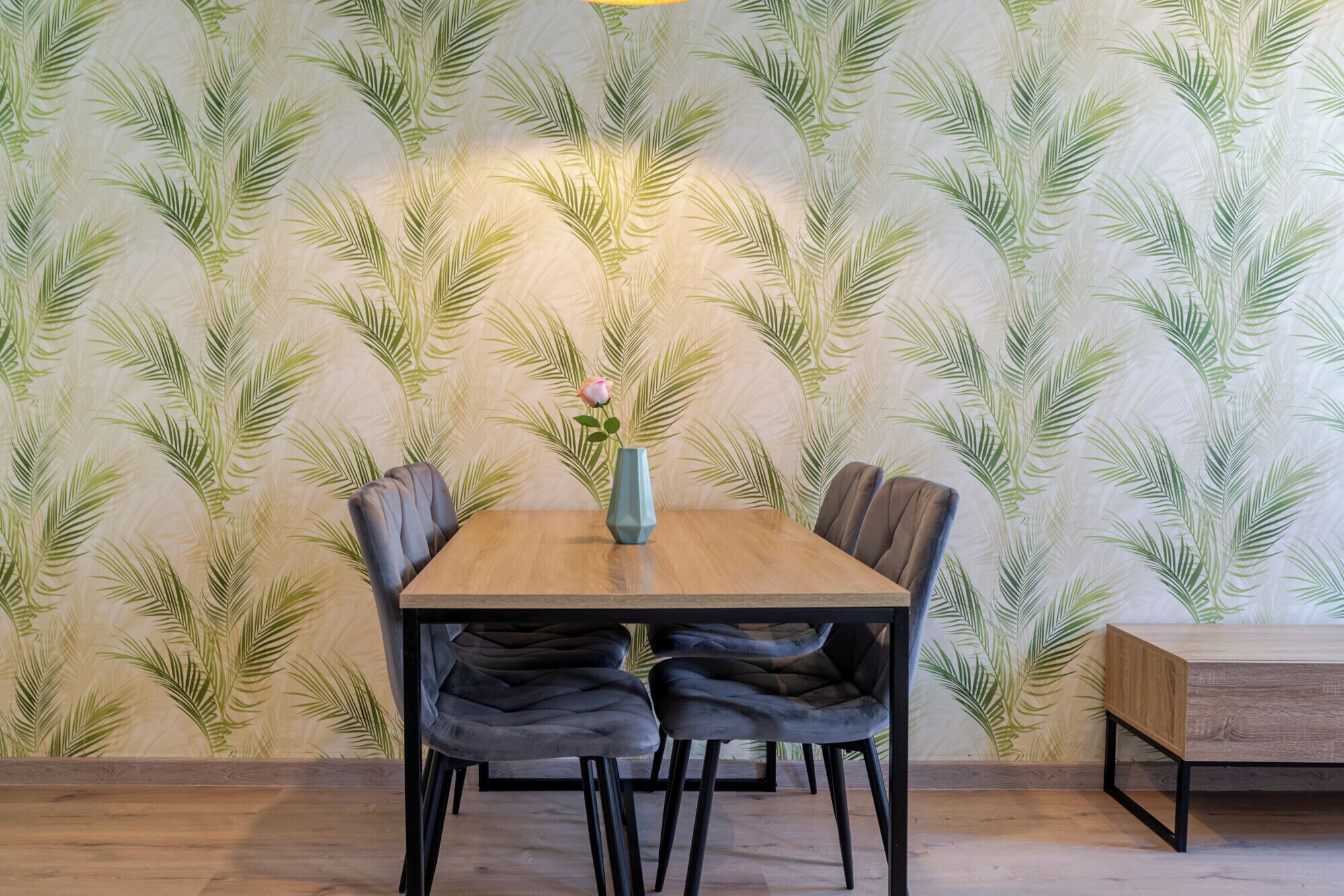 A dining area with a wooden table, four chairs, and a vase with a flower.