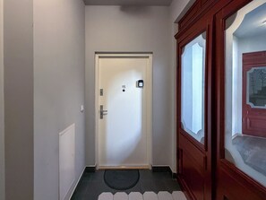Un couloir avec une porte portant le numéro « 15 », un paillasson et une porte en bois dotée d’un panneau de verre.