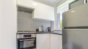 A compact kitchen with white cabinets, a stainless steel refrigerator, a gas stove, and a kettle. - Morawa Pond Comfort Studio (Katowice)