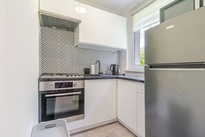 Eine kompakte Küche mit weißen Schränken, einem Edelstahlkühlschrank, einem Gasherd und einem Wasserkocher.