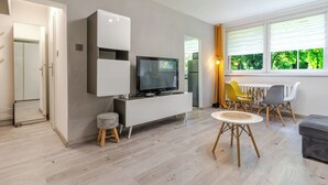A modern living room with a flat-screen TV, a dining area with a table and chairs, and a window with blinds. - Morawa Pond Comfort Studio (Katowice)