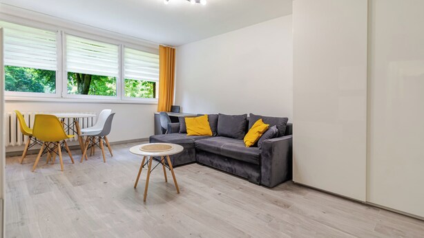 A modern living room with a grey sofa, yellow cushions, a round coffee table, and a dining area with a white table and yellow chairs. - Morawa Pond Comfort Studio (Katowice)
