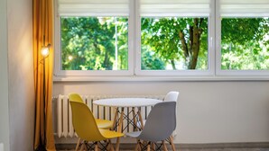 A room with a round table, two chairs, a floor lamp, and a view of greenery through a window with blinds. - Morawa Pond Comfort Studio (Katowice)
