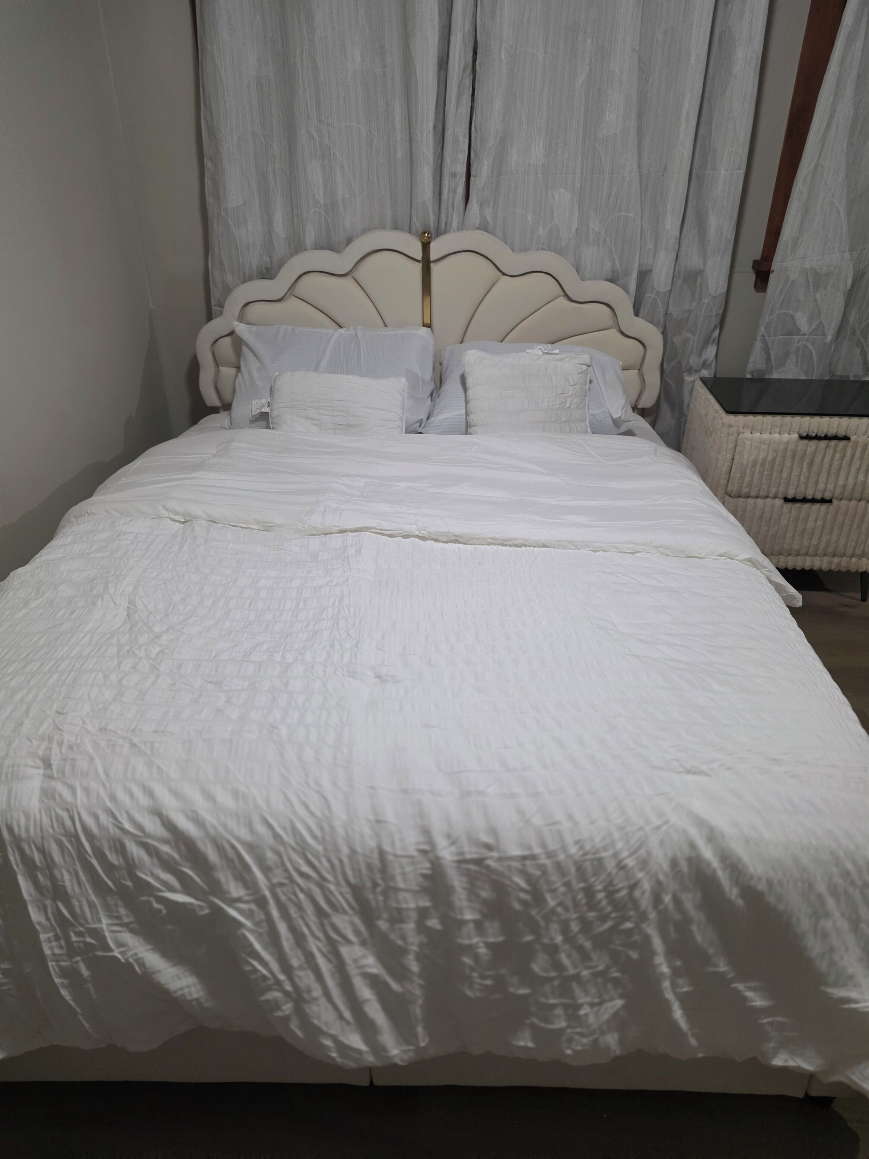 Uma cama com cabeceira, roupa de cama branca e mesa de cabeceira com uma cesta.