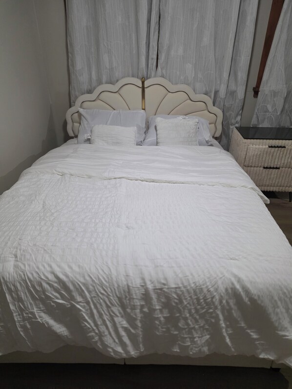 A bed with a headboard, white bedding, and a bedside table with a basket.