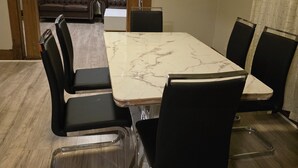 Een eetgedeelte met een marmeren tafel en zwarte stoelen, een bruine leren bank en een houten deuropening naar een balkon.