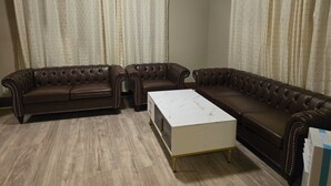 Een woonkamer met twee bruine leren banken, een witte salontafel en lichte gordijnen.