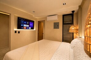 A hotel room with a bed, a mounted TV displaying various streaming services, an air conditioning unit, and a textured wall lamp. - Water-front Luxury + King Bed w/AC (Tijuana)