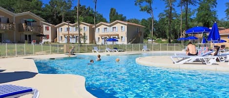 A swimming pool with lounge chairs and umbrellas, surrounded by buildings with balconies.