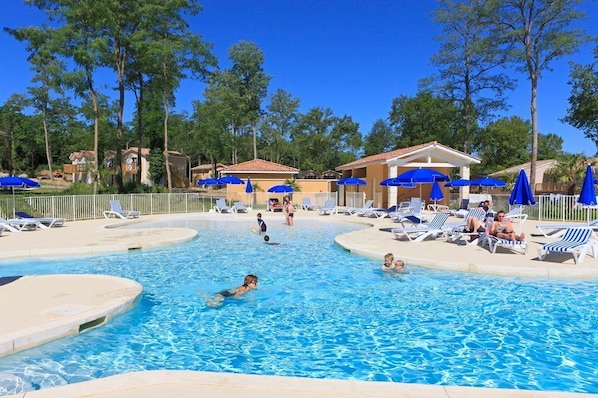 A swimming pool with lounge chairs and umbrellas, surrounded by trees and buildings.