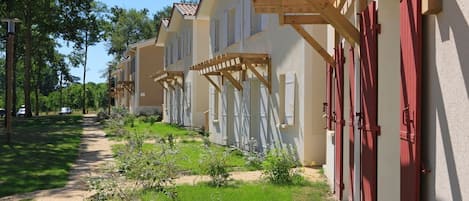 Una hilera de casas con balcones de madera y contraventanas rojas, rodeadas de vegetación y un cielo despejado.