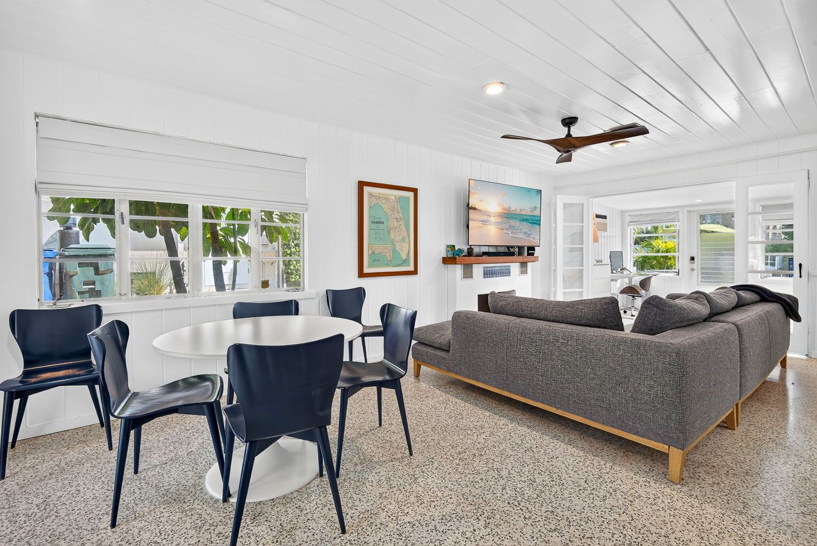 A modern living room with a round table, chairs, a sofa, and a ceiling fan.