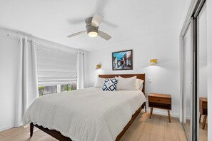 A bedroom with a bed, a ceiling fan, a window with blinds, a bedside table, and a wall-mounted lamp. - Pet Friendly Canal Home - Boat Lift + Paddleboards (Sarasota)