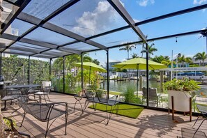 A covered outdoor area with a view of a marina, featuring tables and chairs, umbrellas, and a water body. - Pet Friendly Canal Home - Boat Lift + Paddleboards (Sarasota)