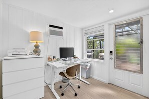 A white-paneled room with a desk, a computer, a lamp, and a window with a view of greenery. - Pet Friendly Canal Home - Boat Lift + Paddleboards (Sarasota)