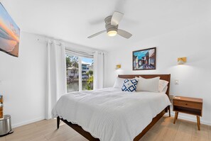 A bedroom with a bed, a ceiling fan, a nightstand, and a view of the outdoors. - Pet Friendly Canal Home - Boat Lift + Paddleboards (Sarasota)