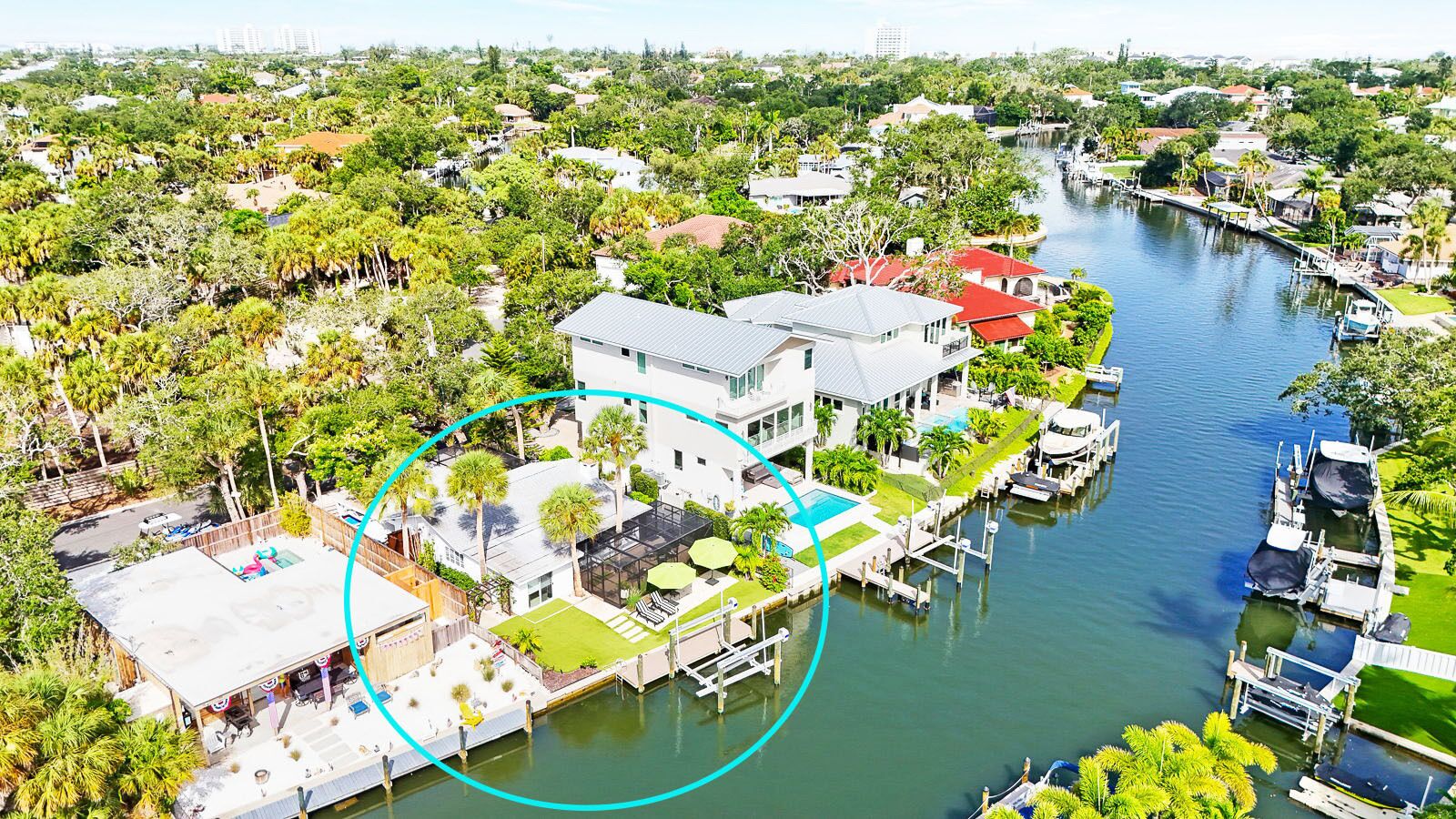 An aerial view of a residential area with a house featuring a pool, dock, and lush greenery.