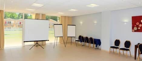 Un salón de conferencias con dos pizarras blancas, una fila de sillas y vistas a un patio de juegos desde las ventanas.
