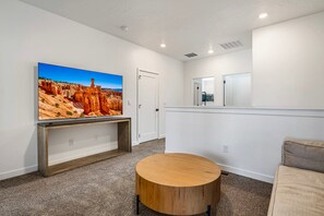 Une pièce dotée d’un téléviseur à écran plat fixé au mur, d’une console en bois, d’une table ronde en bois et d’un miroir placé au-dessus d’une porte.