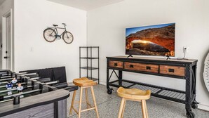 A room with a foosball table, a bicycle mounted on the wall, a TV on a wooden cabinet, and a metal shelf unit. - 3819, Private Pool, Private Spa, BBQ, Outdoor Fire Pit, Xbox 1 (Hurricane)