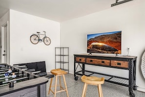 A room with a foosball table, a bicycle mounted on the wall, a TV on a wooden cabinet, and a metal shelf unit. - 3819, Private Pool, Private Spa, BBQ, Outdoor Fire Pit, Xbox 1 (Hurricane)
