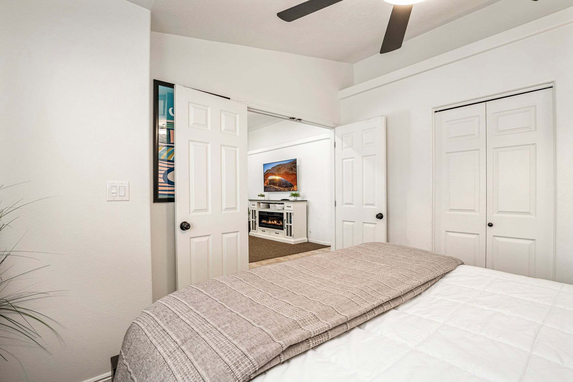 A bedroom with a bed, a ceiling fan, a fireplace, and a TV.