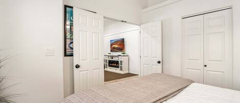 A bedroom with a bed, a ceiling fan, a fireplace, and a TV.