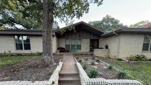 A two-story brick house with a front porch, a tree, and a pathway leading to the entrance. - Spacious 4-bedroom house near DFW (Euless)