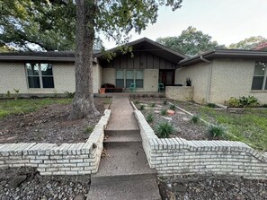 A two-story brick house with a front porch, a tree, and a pathway leading to the entrance. - Spacious 4-bedroom house near DFW (Euless)