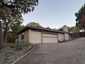 A single-story building with a garage, surrounded by trees and a gravel driveway. - Spacious 4-bedroom house near DFW (Euless)