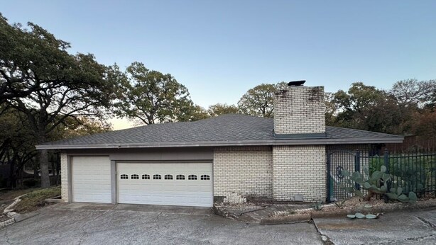 A single-story building with a garage, a brick chimney, and a fenced area with cacti. - Spacious 4-bedroom house near DFW (Euless)