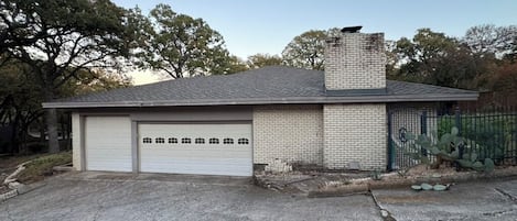A single-story building with a garage, a brick chimney, and a fenced area with cacti.