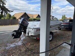 A boat on a trailer with a visible outboard motor, parked on a street with houses in the background.