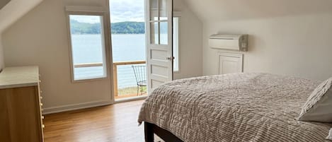 A bedroom with a large bed, a wooden dresser, a window with a view of a lake, and a ceiling fan.