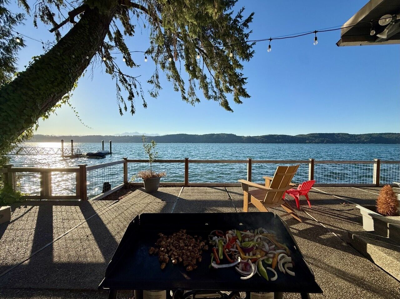 Une terrasse extérieure équipée d’un barbecue, de sièges et offrant une vue sur un lac.