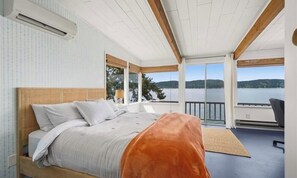 A bedroom with a bed, a view of a lake, and a balcony with a chair.