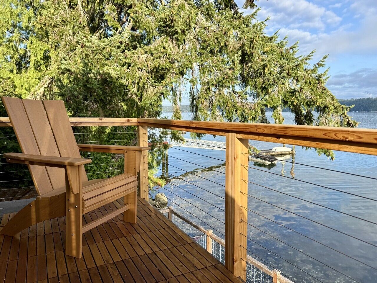 A wooden deck with a chair, overlooking a body of water with a bridge in the distance.