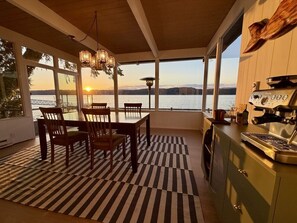 A dining area with a view of a lake and mountains, a kitchen with a coffee machine, and a striped rug.