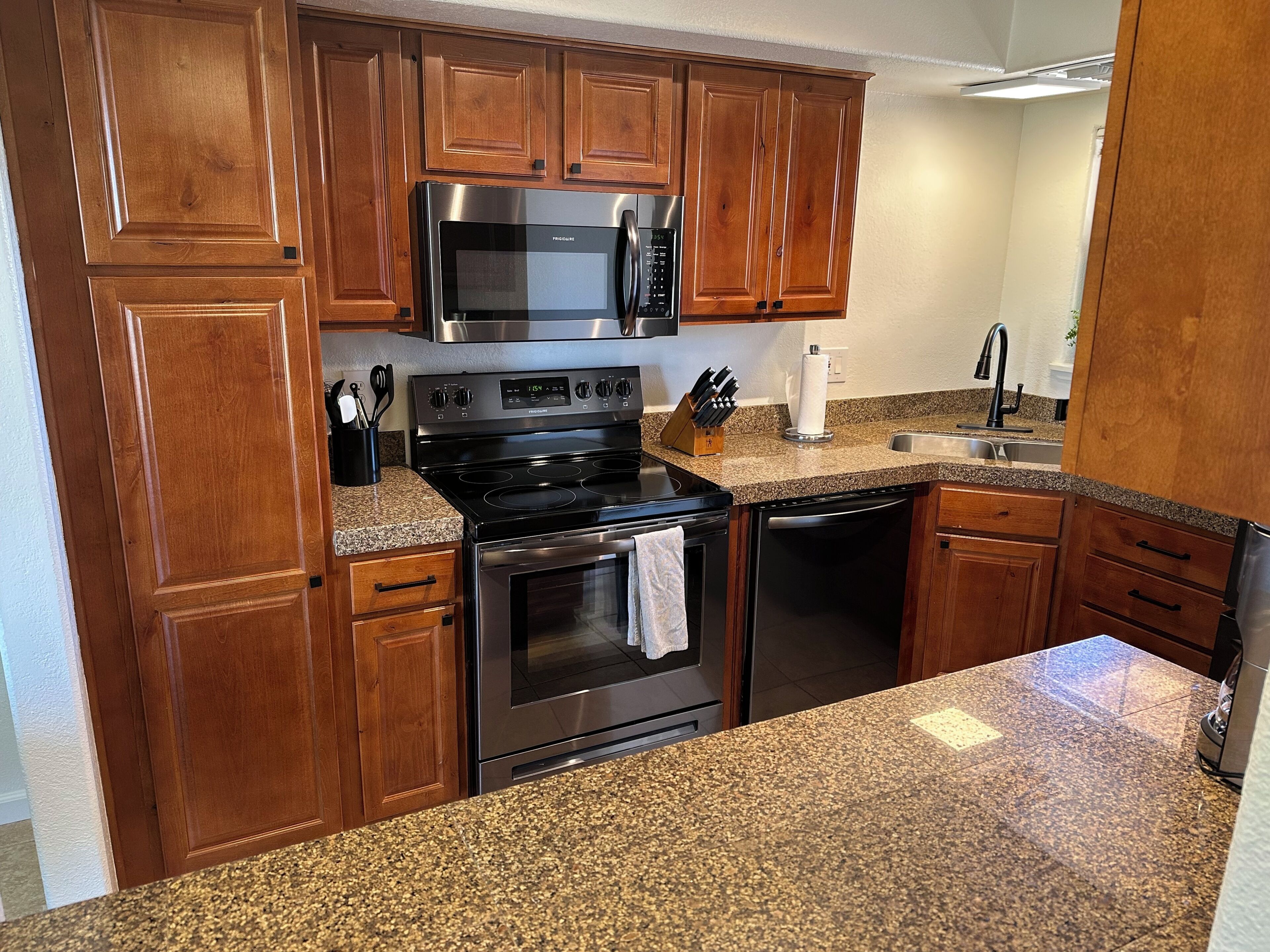 A kitchen with wooden cabinets, a stainless steel stove, a microwave, and granite countertops.