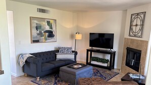 A living room with a dark sofa, a coffee table, a flat-screen TV, a fireplace, and a patterned rug. - Foothills gem! (Tucson)