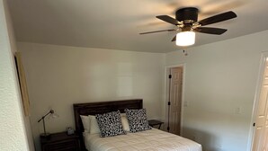 A bedroom with a bed, a nightstand, a lamp, a ceiling fan, and a door. - Foothills gem! (Tucson)