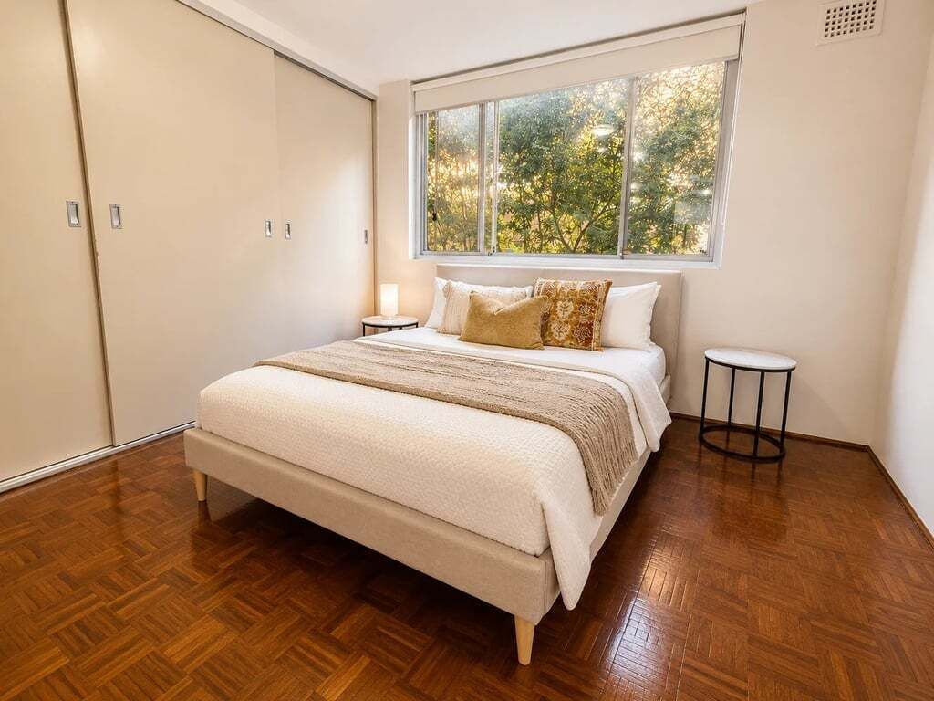 A bedroom with a large bed, a window with a view of trees, and a wardrobe.