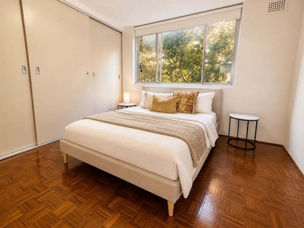 A bedroom with a large bed, a window with a view of trees, and a wardrobe.
