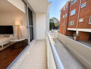 A balcony with a white railing, a flat-screen TV, a lamp, and a small round table.