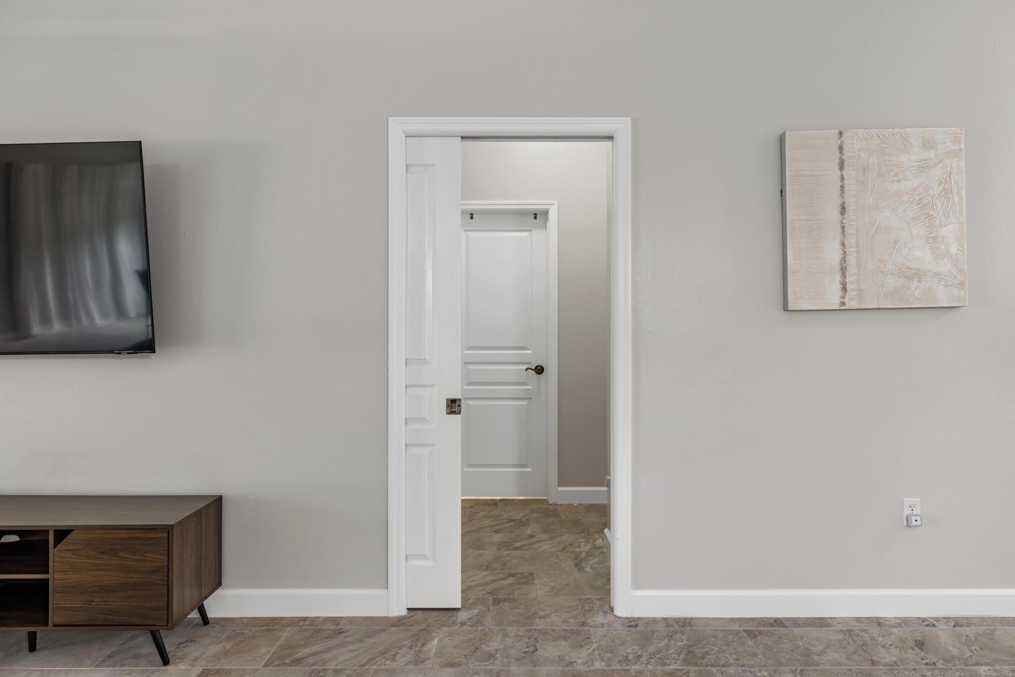 Un couloir avec une porte donnant sur une autre pièce, une œuvre d’art accrochée au mur et un meuble en bois.