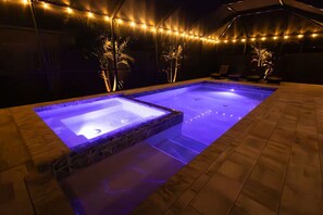 A hot tub with a stone surround and a tiled deck area, surrounded by string lights. - Modern Oasis (Sarasota)