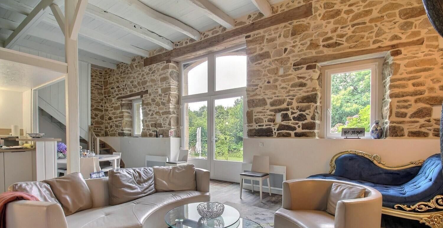 A spacious living area with stone walls, a curved sofa, a blue armchair, and a glass coffee table.