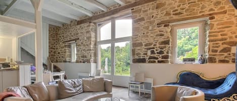 A spacious living area with stone walls, a curved sofa, a blue armchair, and a glass coffee table.